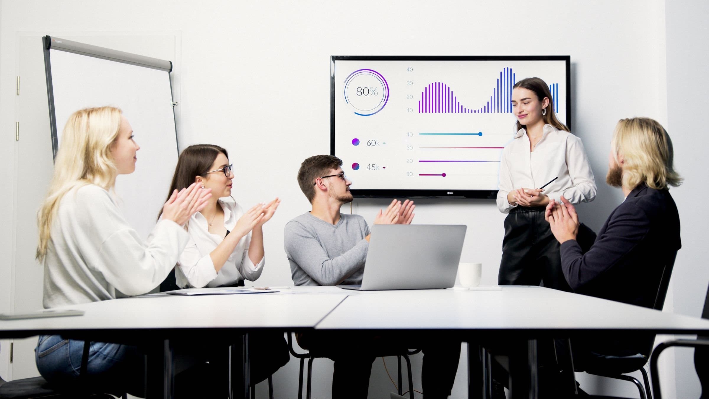 Marketing lead presenting campaign results on a wall screen to an applauding team