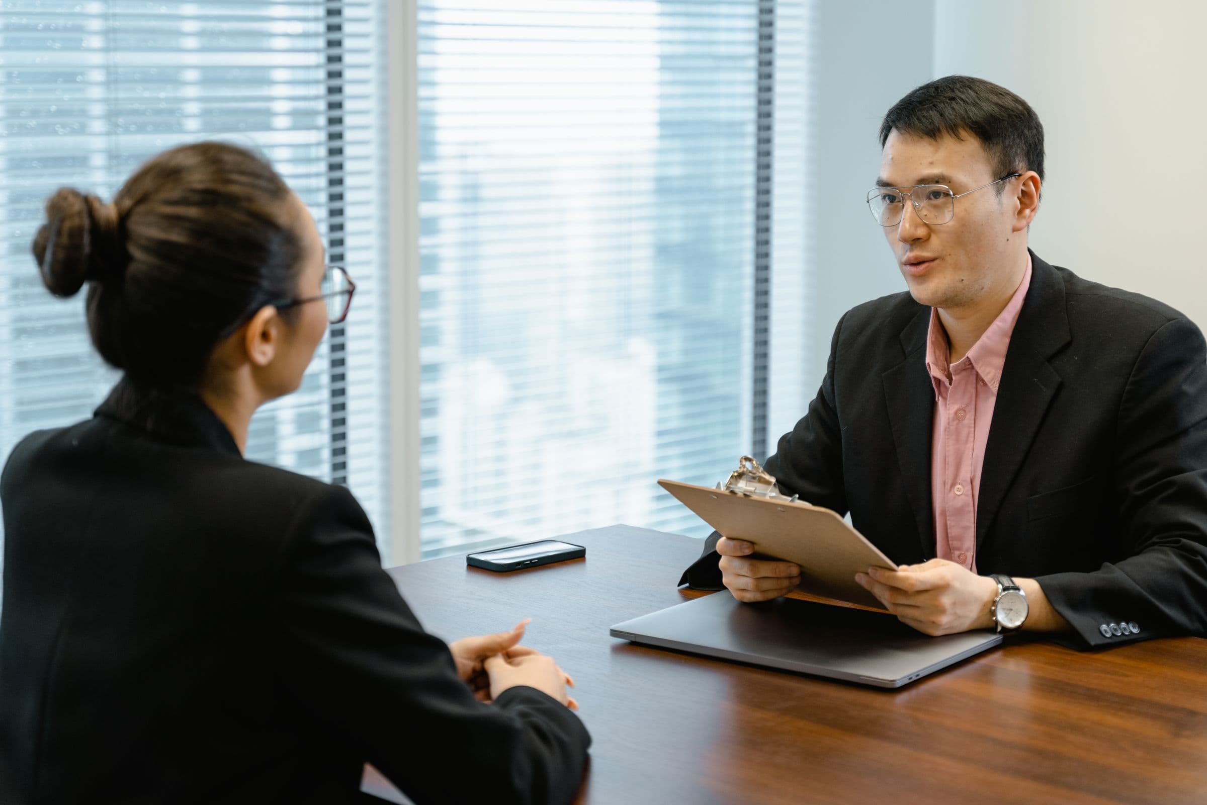 Professional interview across a table in a glass-walled office